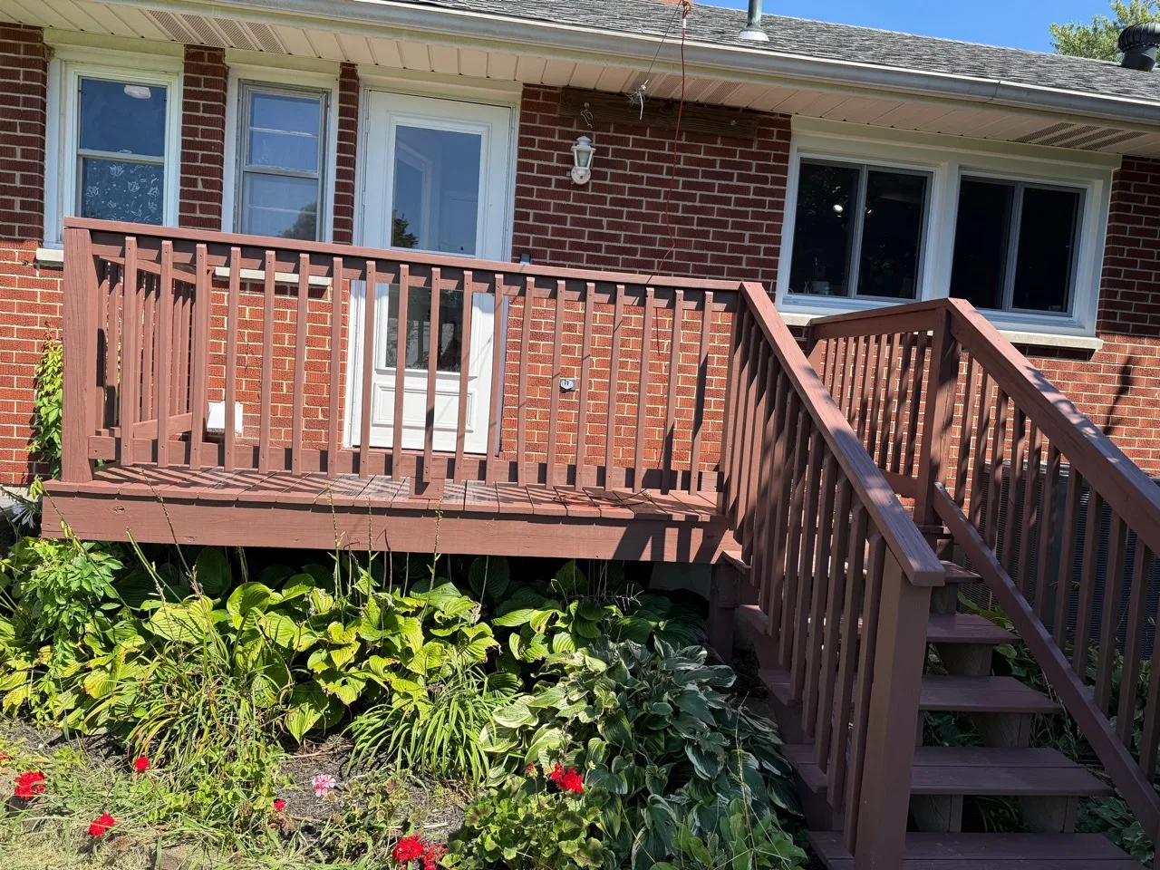 Finished warm-brown deck and railing across the front of a brick home