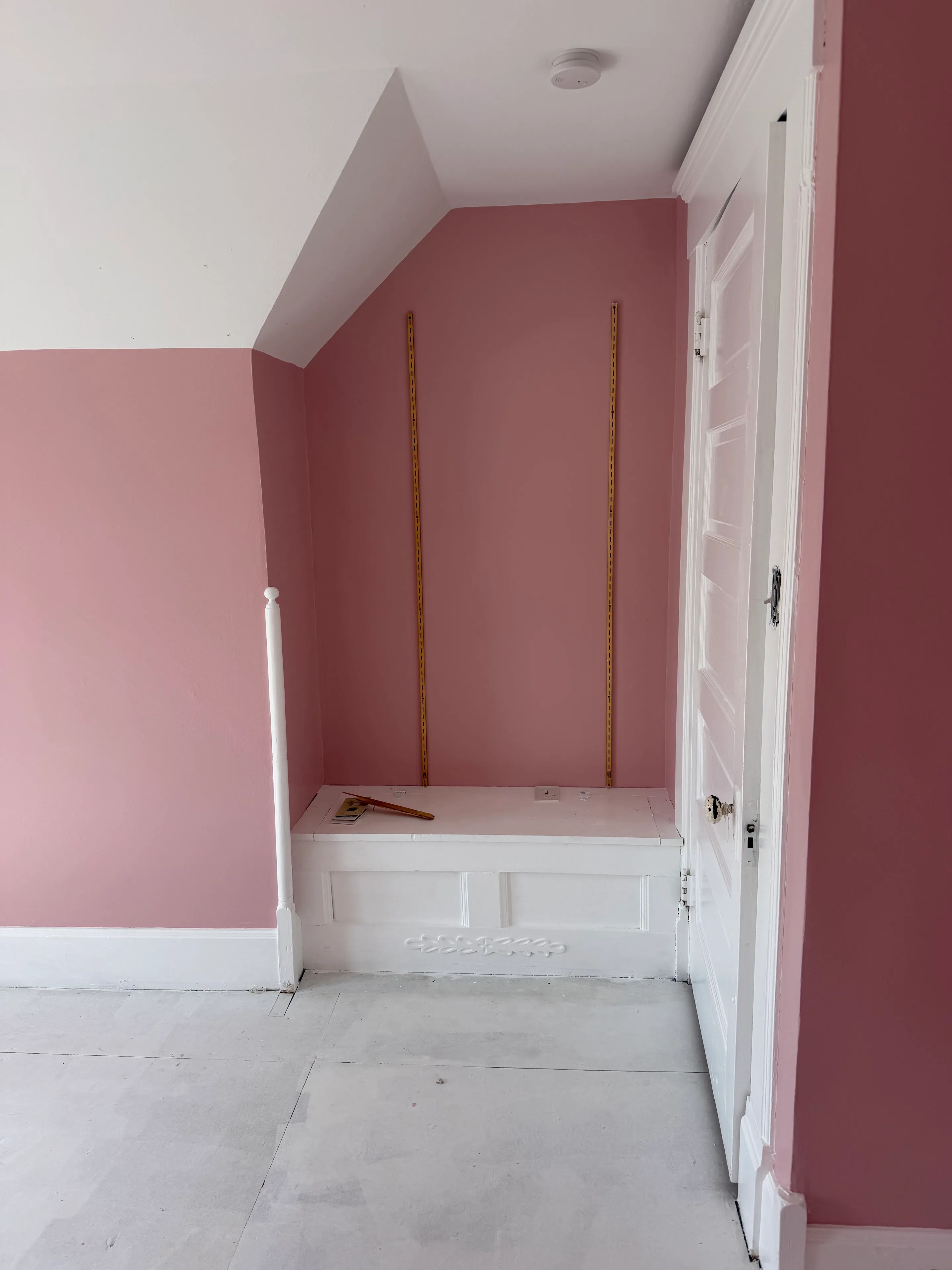 Finished soft-rose wall surrounding a white built-in bench and doorway