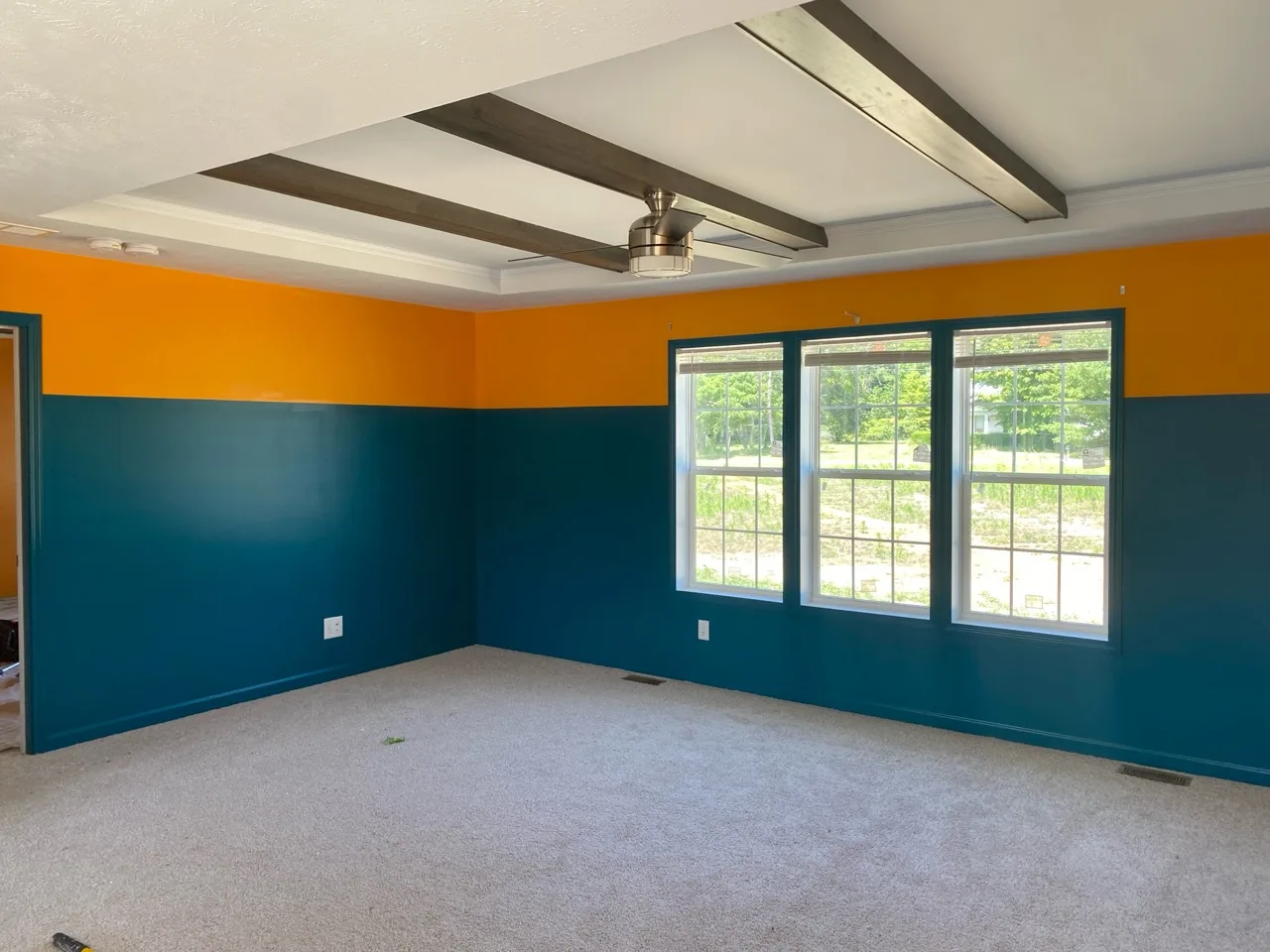 Finished room with deep teal lower walls, golden-orange upper walls, and dark ceiling beams
